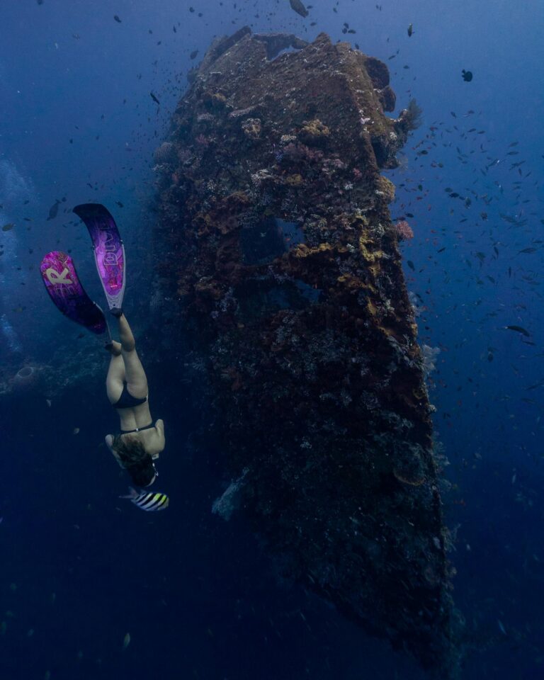 A woman scuba dives near a shipwreck in Bali's vibrant underwater scenery.